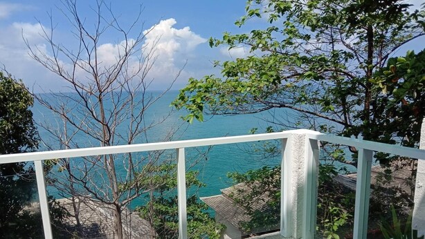 Een balkon met uitzicht op de zee en omliggende bomen.