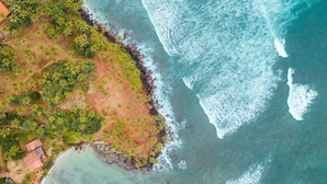 An aerial view of a coastal area with a beach, palm trees, and a rocky shoreline. - Triple O Six (Mirissa)
