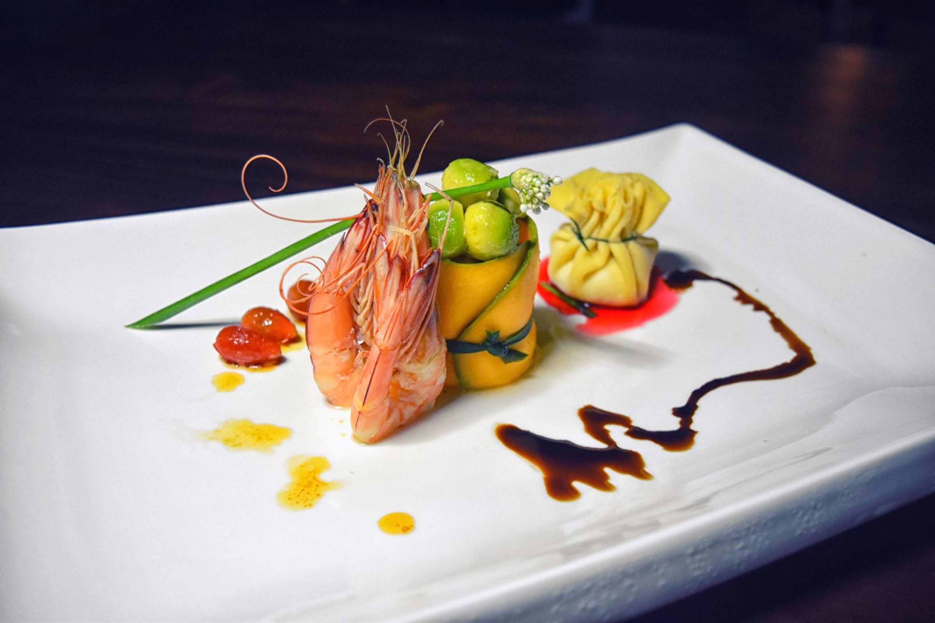 A white rectangular plate with a shrimp, a fruit arrangement, and a small dollop of sauce.