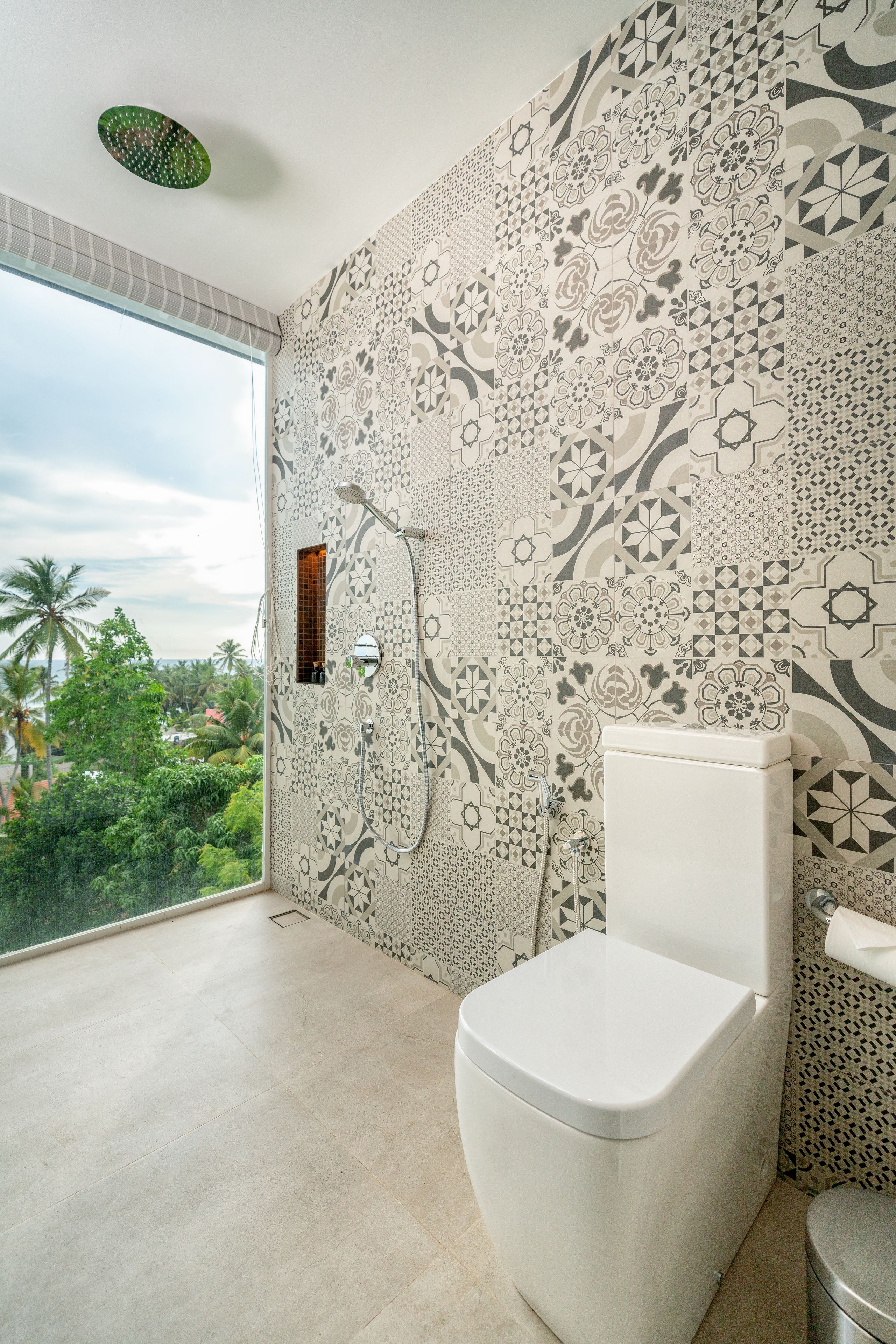 Un baño con inodoro, ducha y un amplio ventanal con vistas a palmeras.