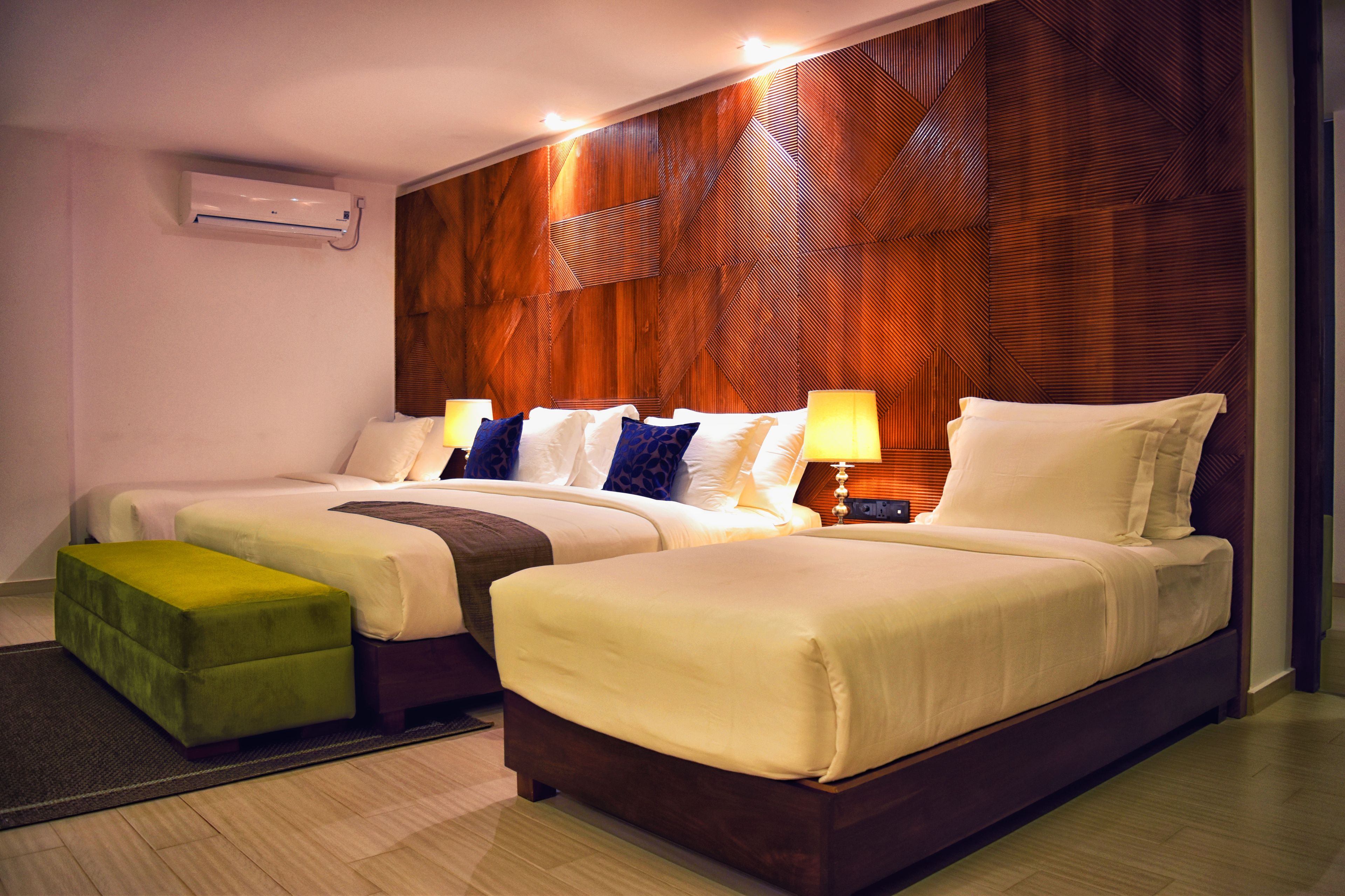 Una habitación de hotel con dos camas, un reposapiés verde y una pared de acento de madera.