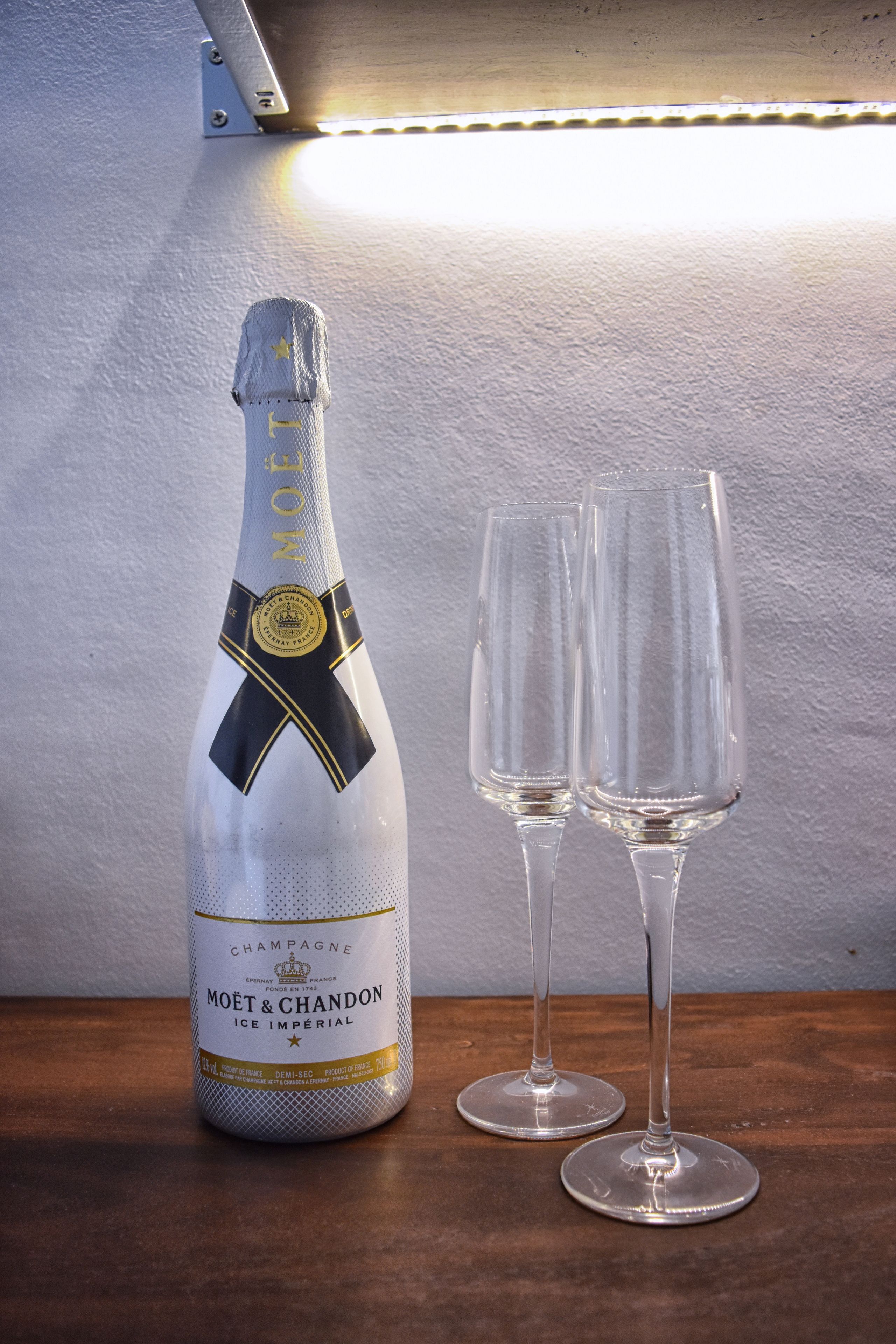 A bottle of Moët & Chandon Ice Imperial champagne and two empty champagne flutes on a wooden table.