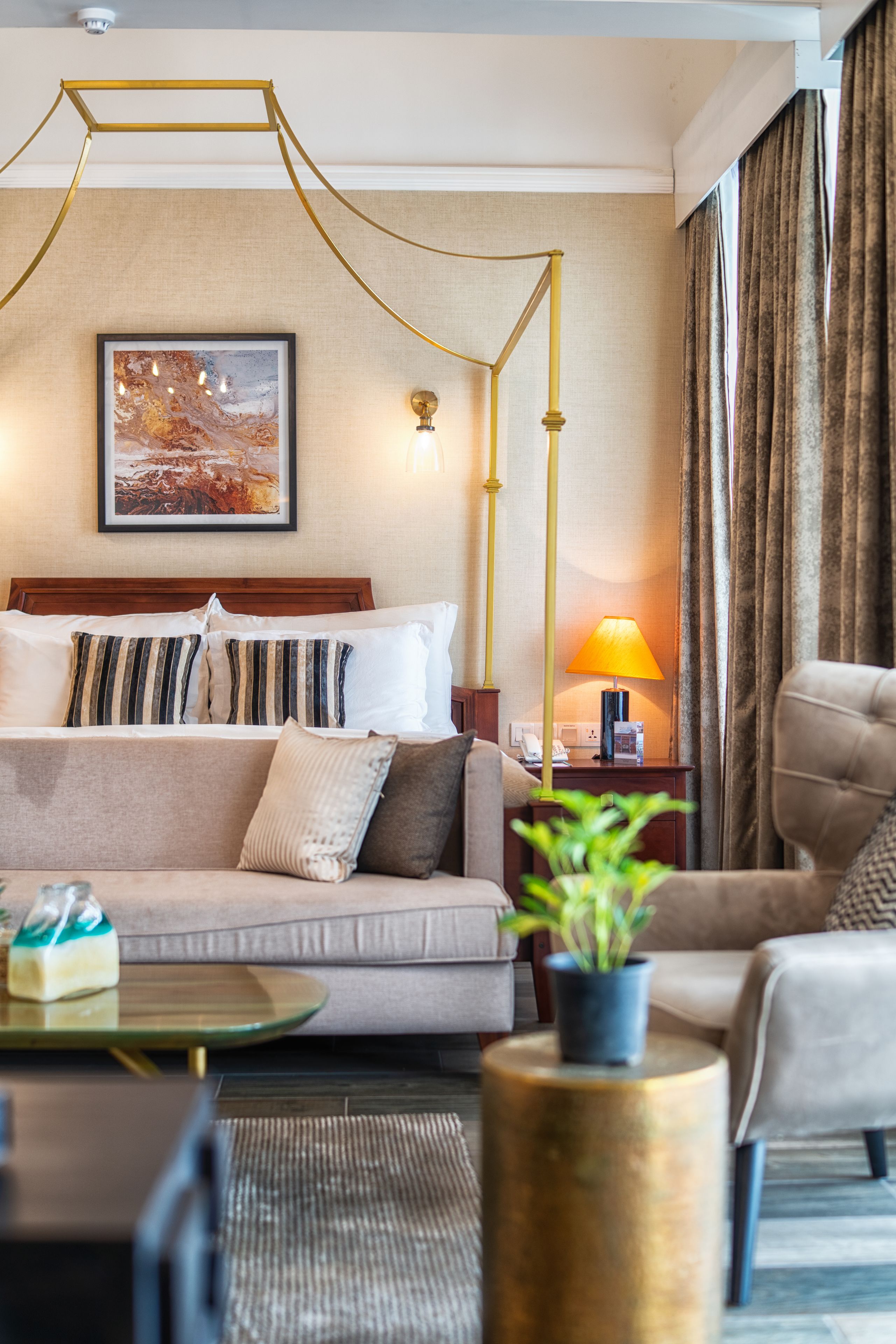 A hotel room with a bed, a sofa, a coffee table, a lamp, and a painting on the wall.