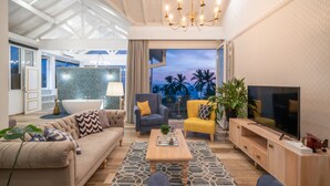 A modern living room with a sofa, armchairs, a coffee table, a TV, and a view of palm trees at dusk. - Triple O Six (Mirissa)
