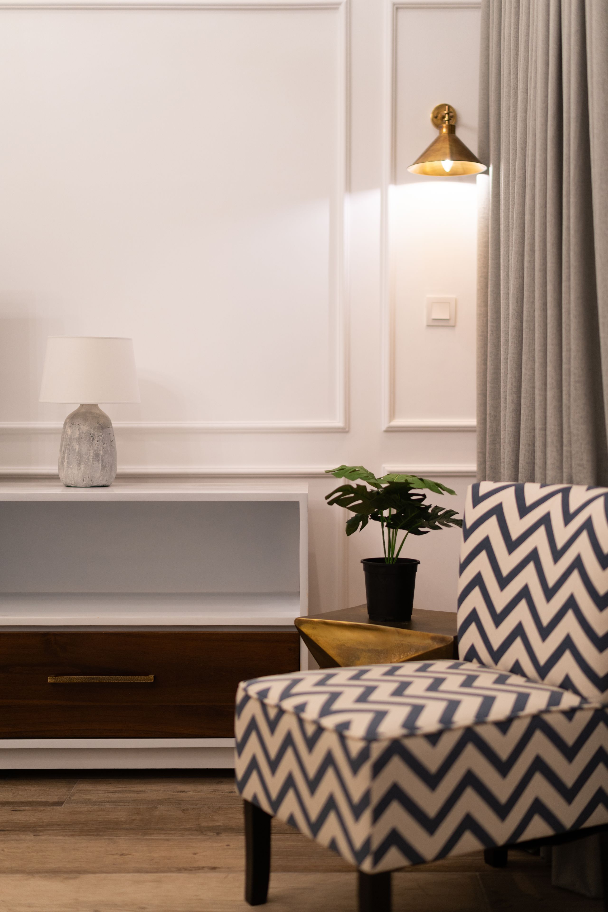 Una sala de estar moderna con un mueble de madera, una lámpara, una planta en maceta y un sillón estampado.