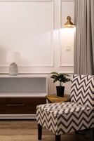 Una sala de estar moderna con un mueble de madera, una lámpara, una planta en maceta y un sillón estampado.