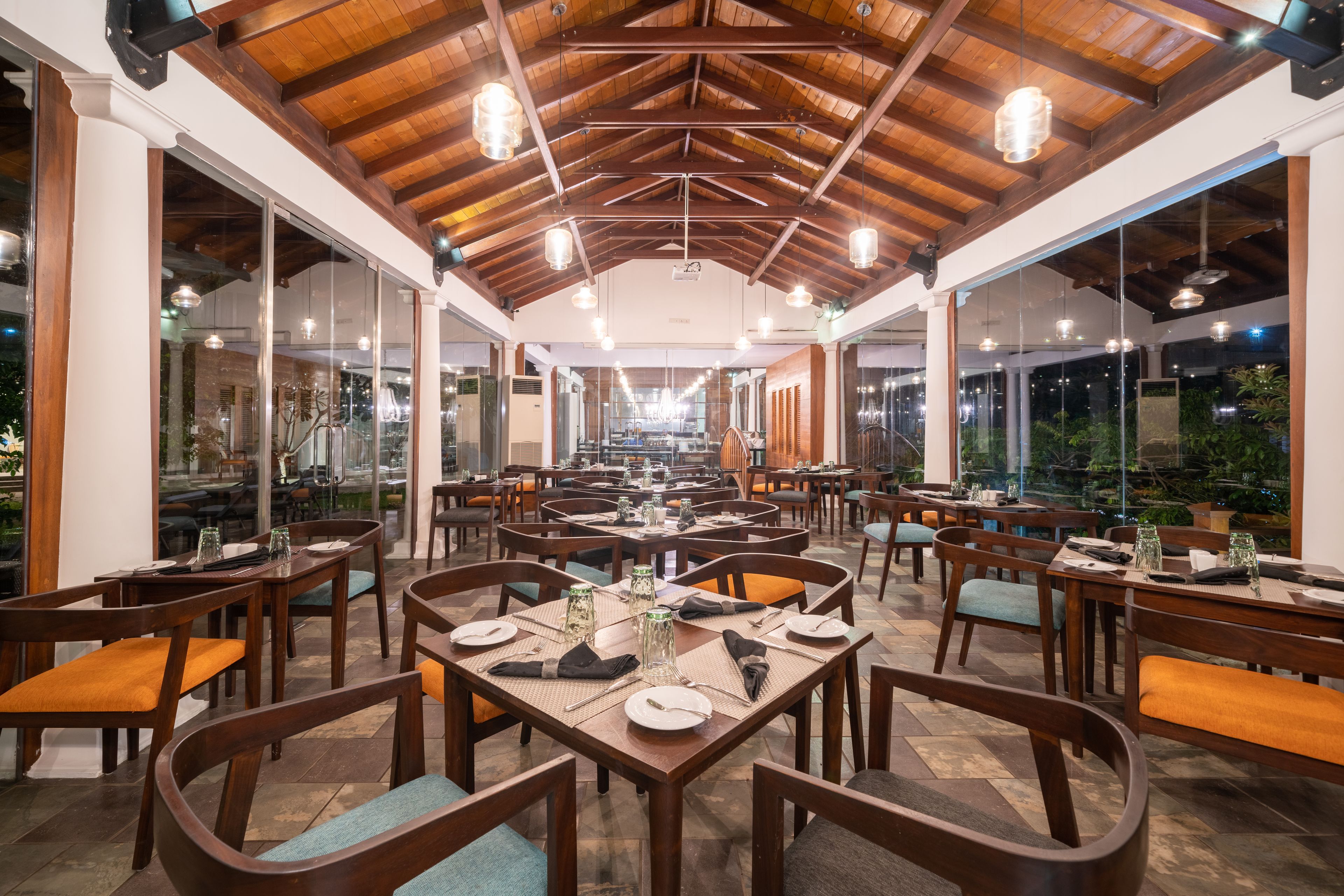 A spacious restaurant with wooden tables and chairs, large windows, and a high wooden ceiling.