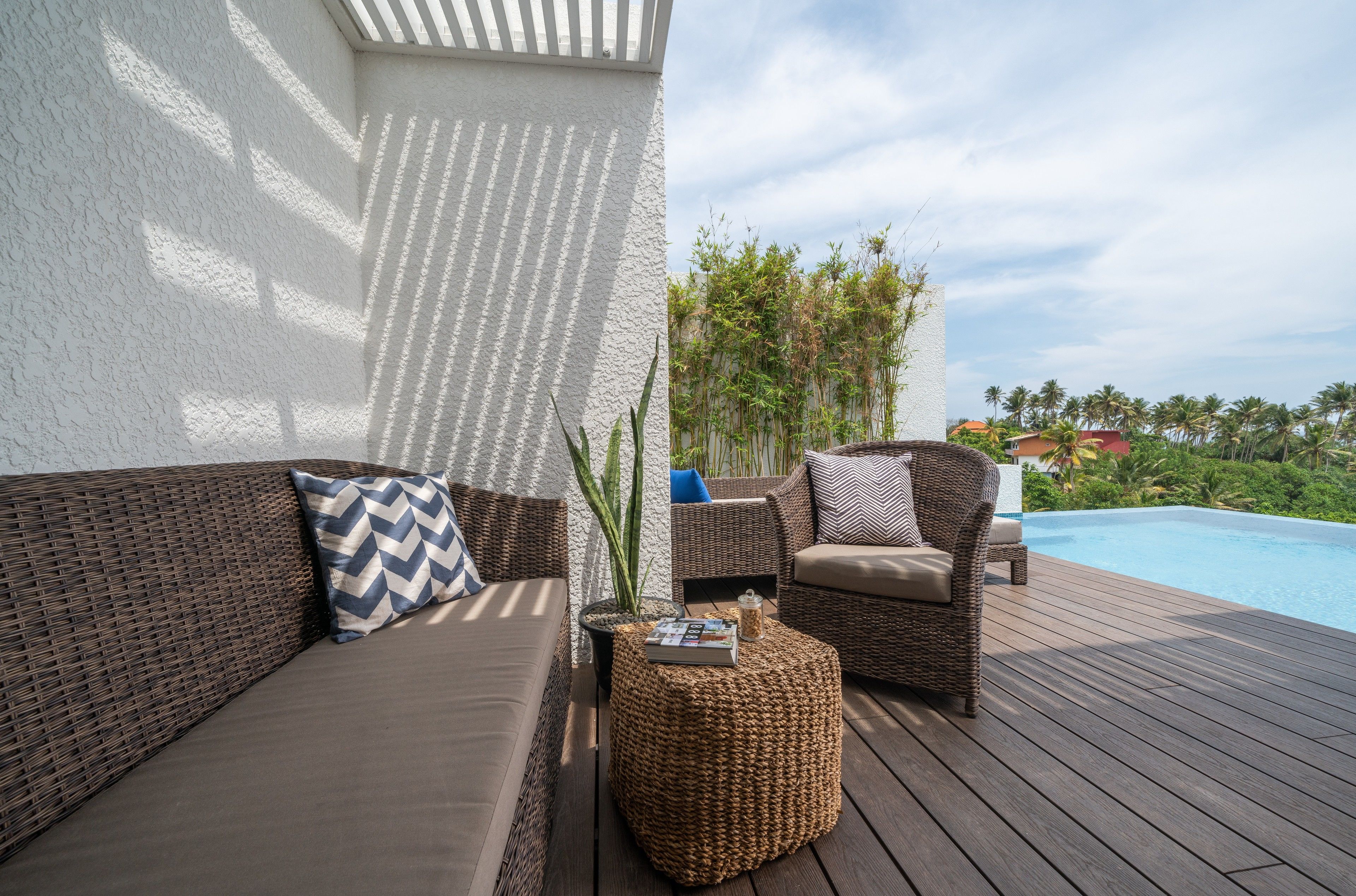 A wooden deck with wicker furniture, a pool, and a white wall.