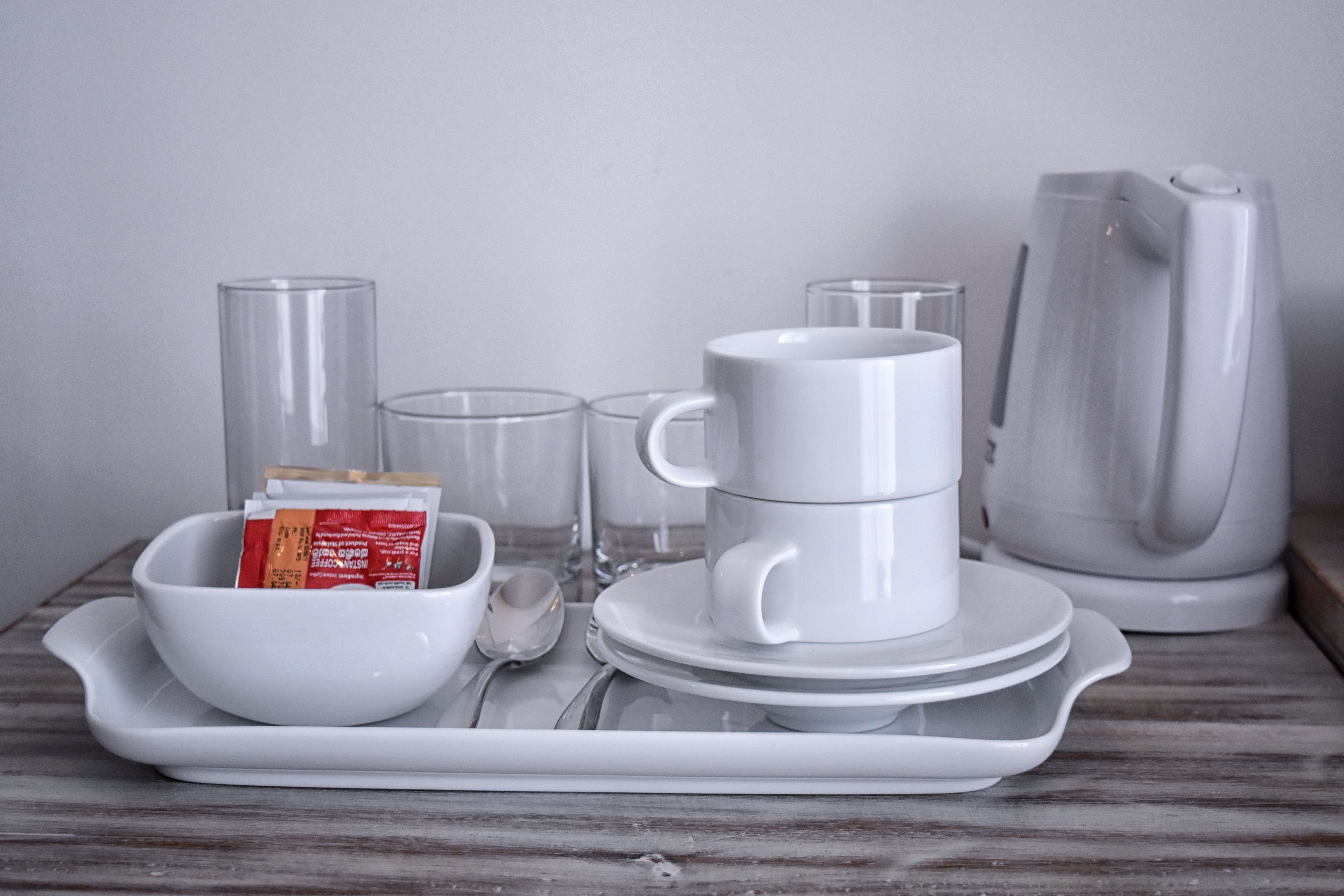 A tray with a white mug, a white cup, a white bowl, and a white teapot on a wooden surface.