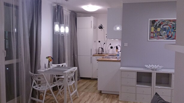 A compact kitchen with white cabinets, a dining table with chairs, and a small countertop with a sink and decorative items.