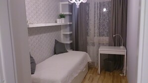 A small bedroom with a bed, a desk, a chair, a shelf with plants, and a curtain.