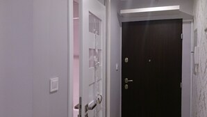 A hallway with a white door leading to a room with pink walls and a shower.