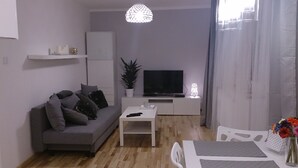 A modern living room with a grey sofa, a white coffee table, a flat-screen TV, a potted plant, and a decorative light fixture.
