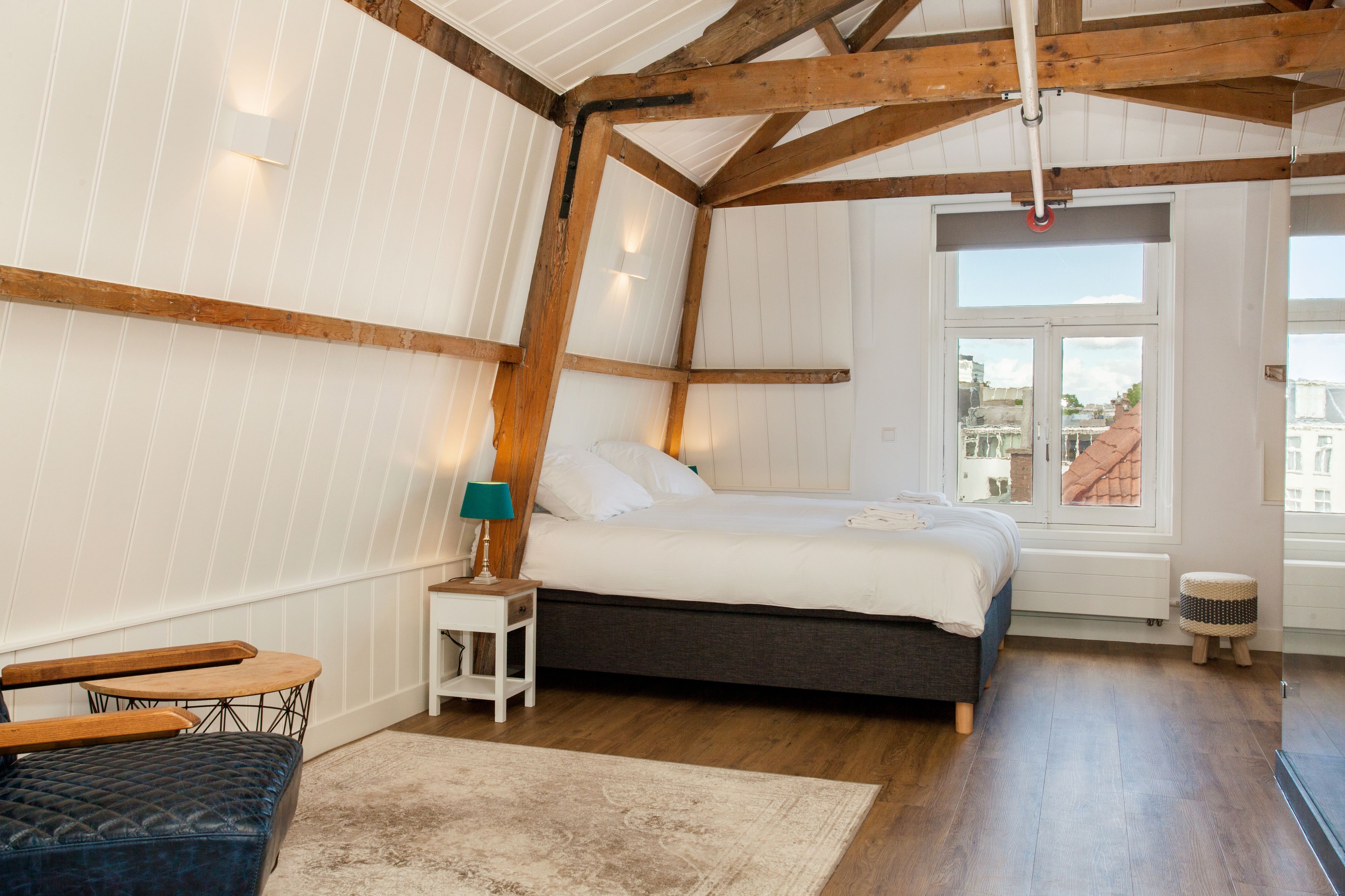 Een slaapkamer met een bed, nachtkastje, lamp en uitzicht.