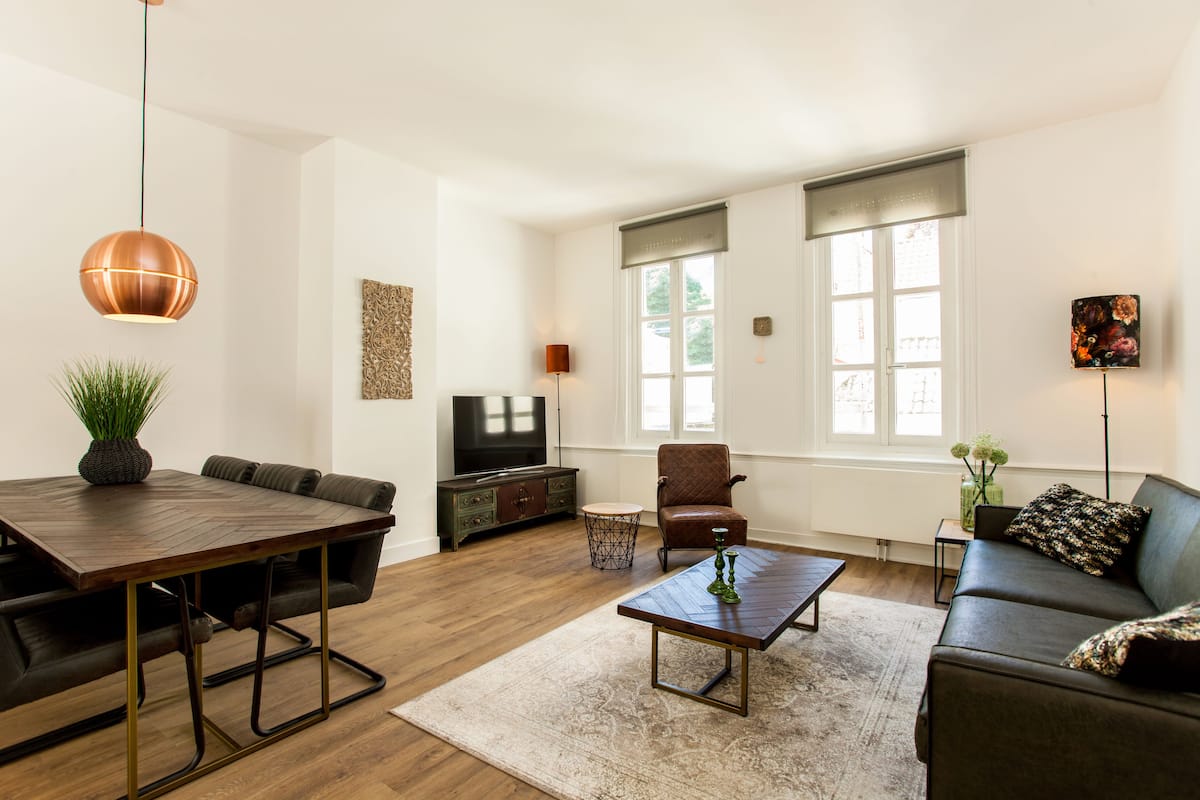 A modern living room with a wooden dining table, leather sofa, and a television.