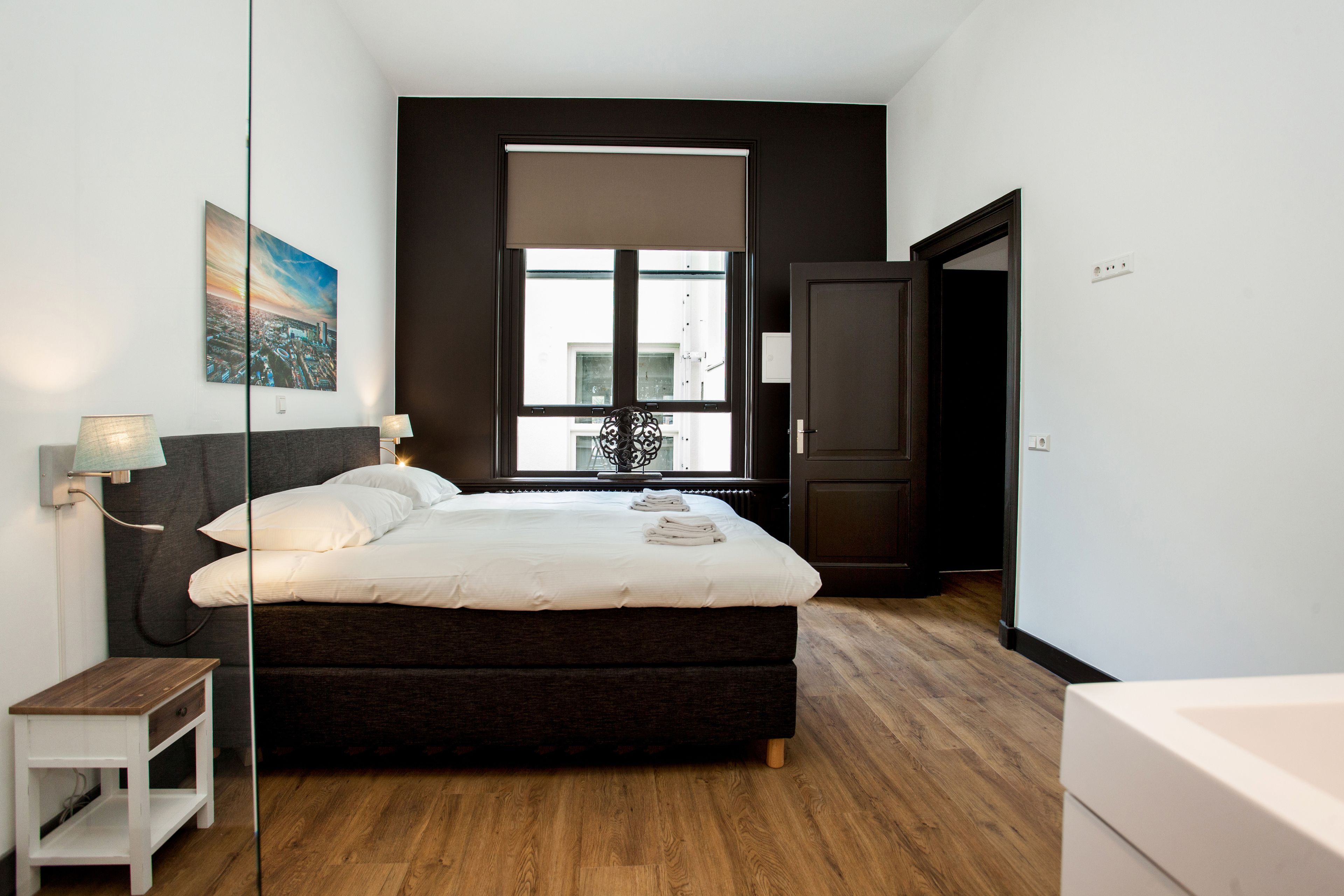 A bedroom with a large bed, a bedside table, a lamp, a window with a view, and a door.