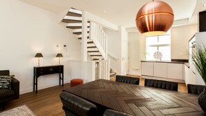 Una sala moderna con una mesa de comedor de patrón espiga, asientos de cuero, una escalera y una cocina al fondo.