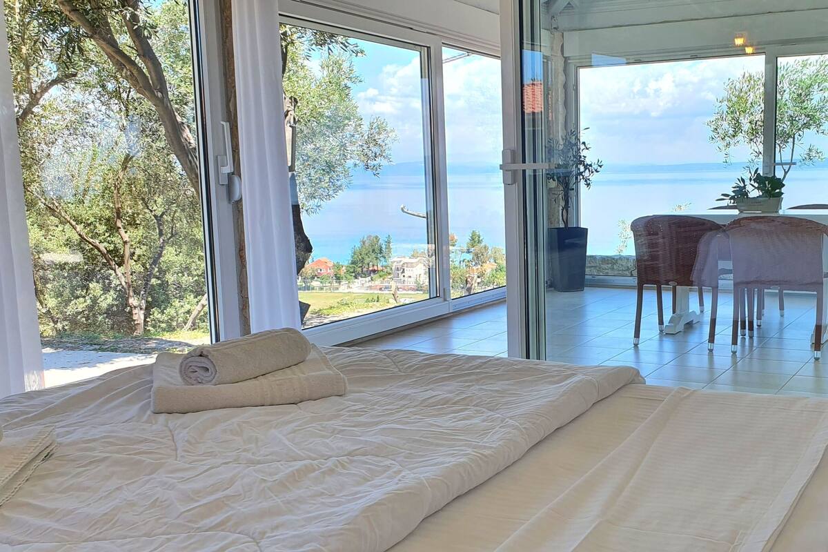 Une chambre avec un grand lit, une vue sur la mer et un balcon équipé d’une table et de chaises.