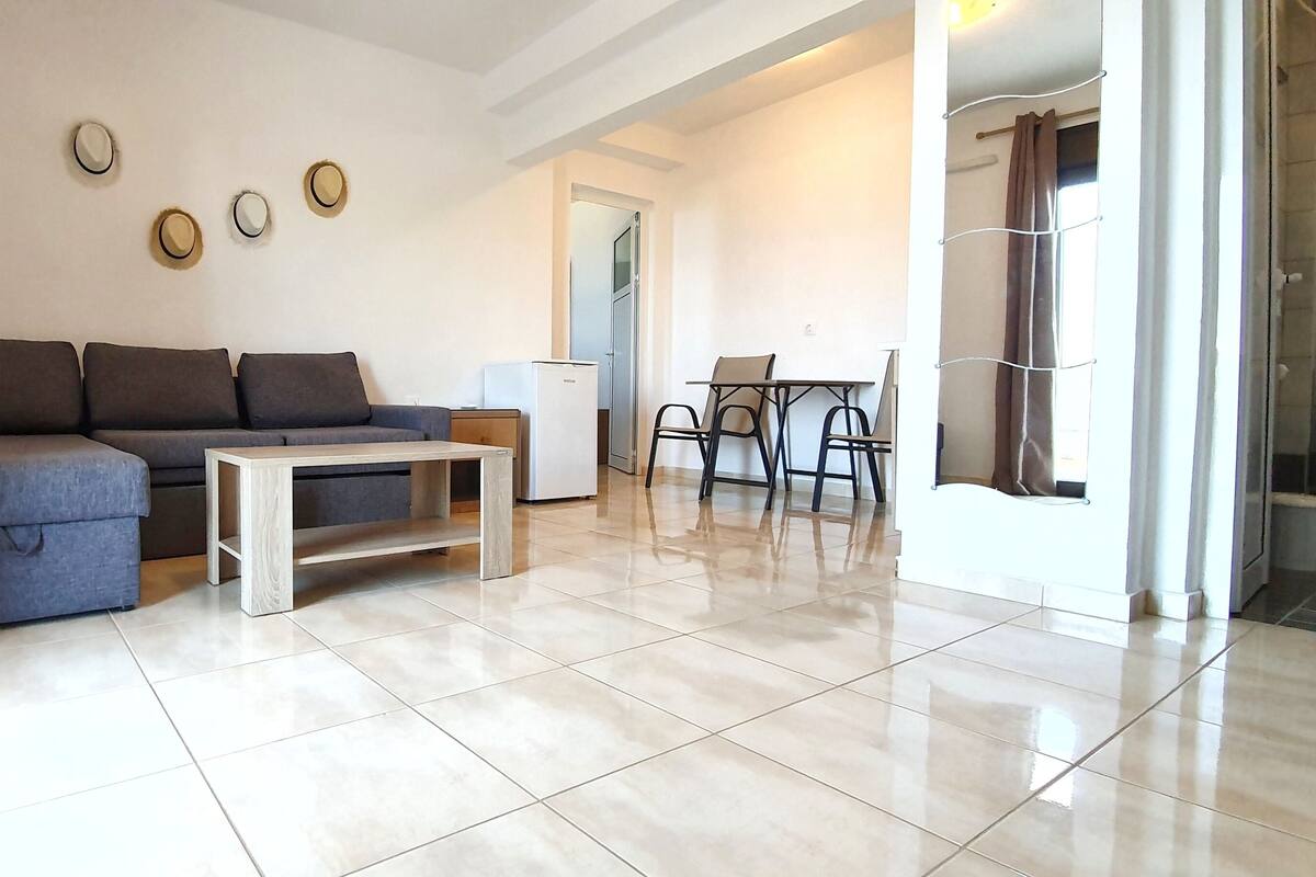 Un salon moderne avec un canapé gris, une table basse blanche et un coin repas comprenant une table et des chaises.