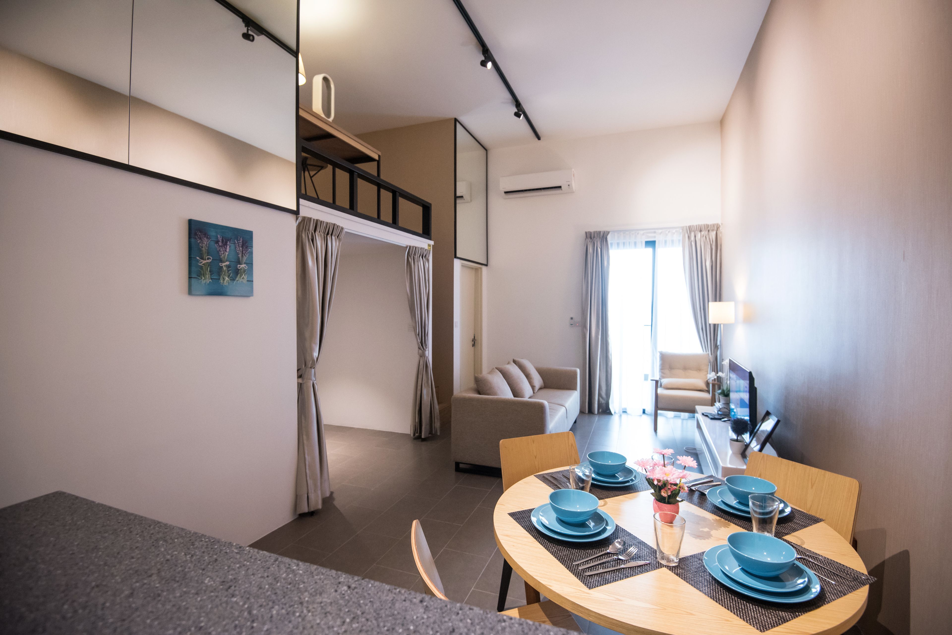 Ein modernes Hotelzimmer mit Essbereich, inklusive rundem Tisch, gedeckt mit blauen Tellern und einer kleinen Blumenvase.