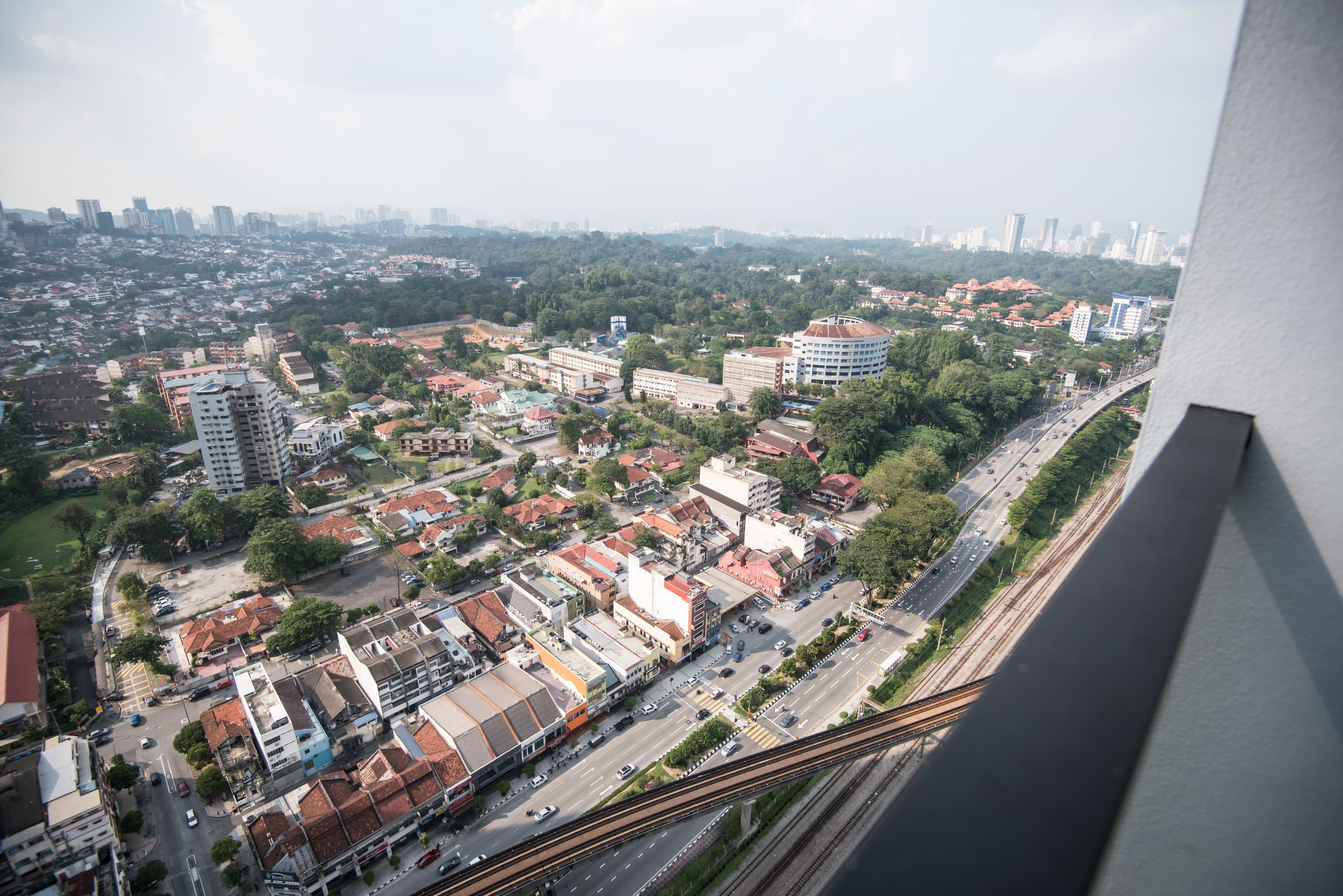 A cityscape with a mix of residential and commercial buildings, a railway track, and a road with vehicles.