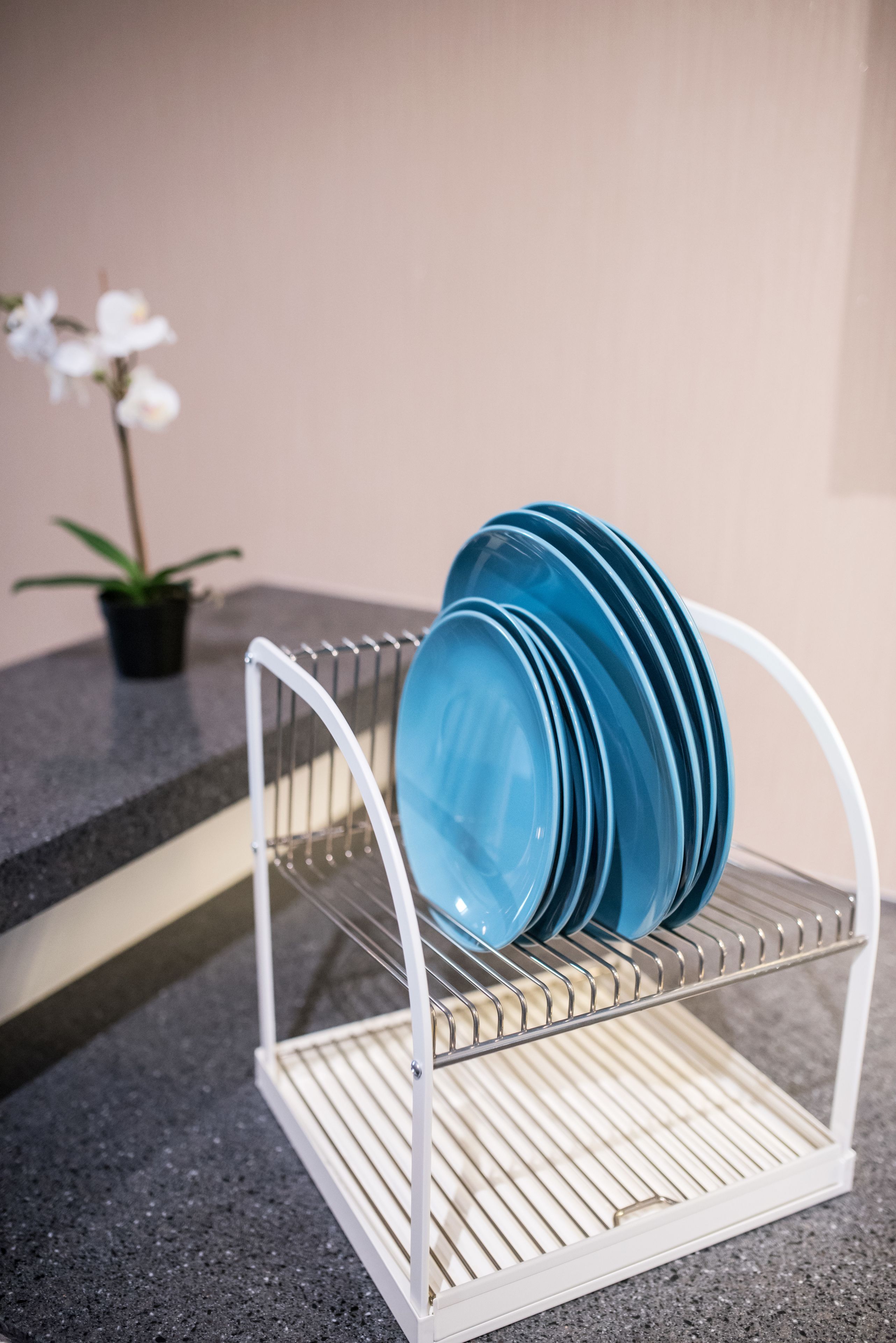 Un égouttoir à vaisselle en métal blanc avec des assiettes bleues, posé sur un comptoir en granit.