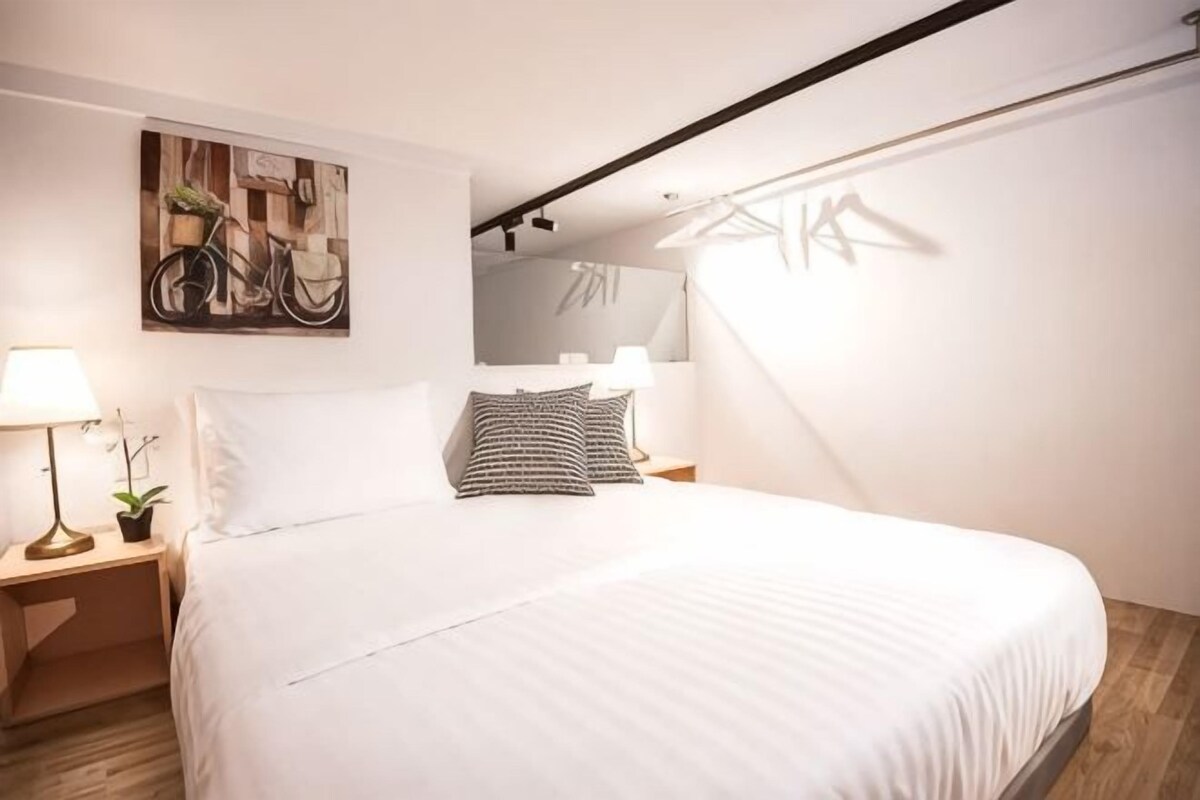 A modern bedroom with a bed, bedside tables, a bicycle painting, and a window.