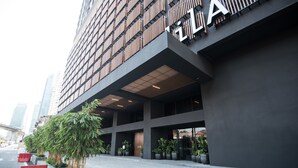 Um edifício moderno com um grande letreiro com a letra 'A', apresentando uma entrada coberta e plantas em vasos ao longo da passarela.