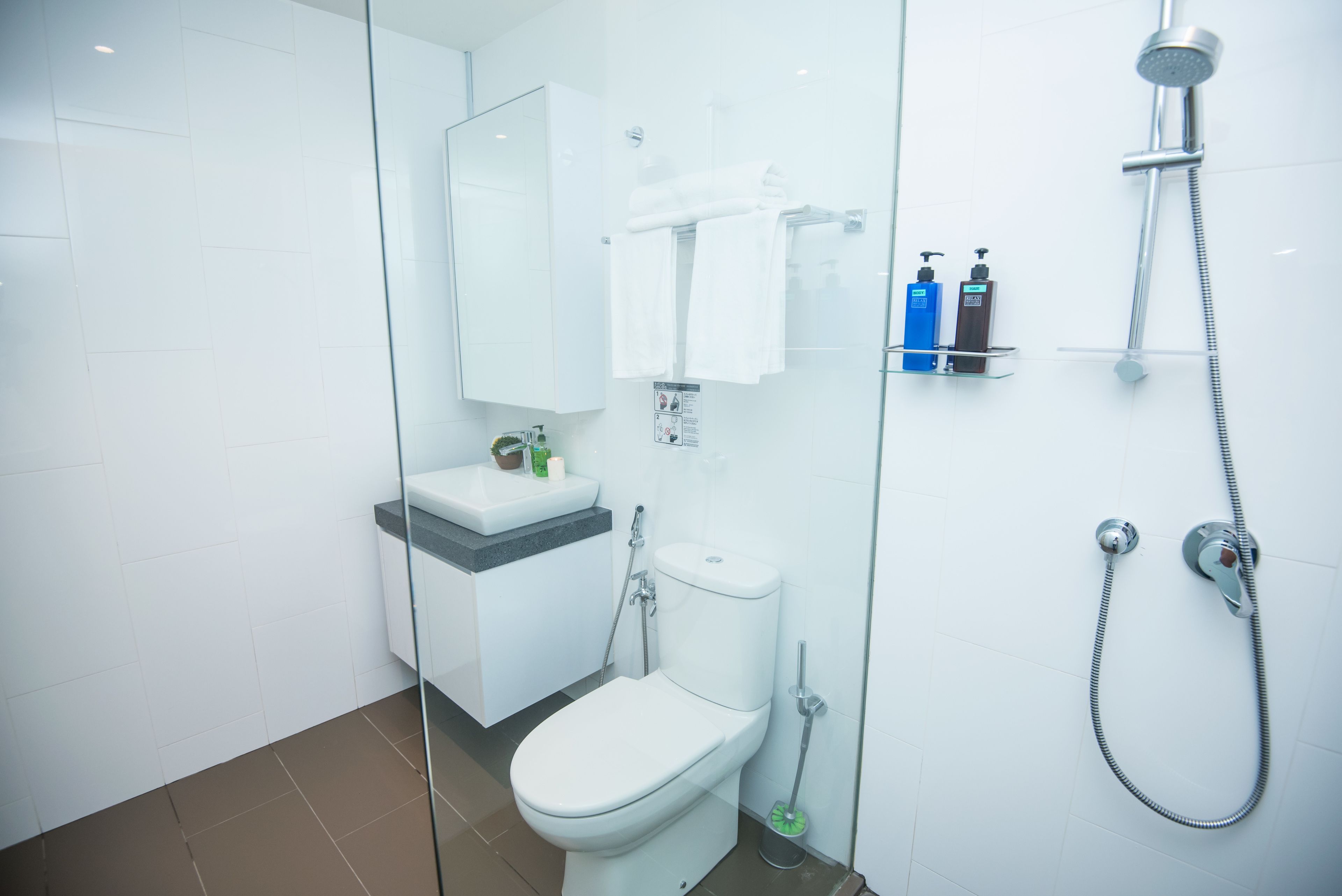 A modern bathroom with a glass shower enclosure, a toilet, and a sink with toiletries.