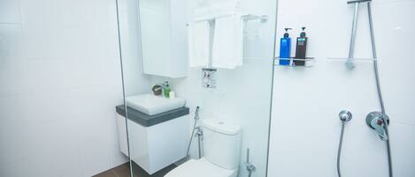 Ein modernes Badezimmer mit Duschkabine aus Glas, Toilette und Waschbecken mit Pflegeprodukten.