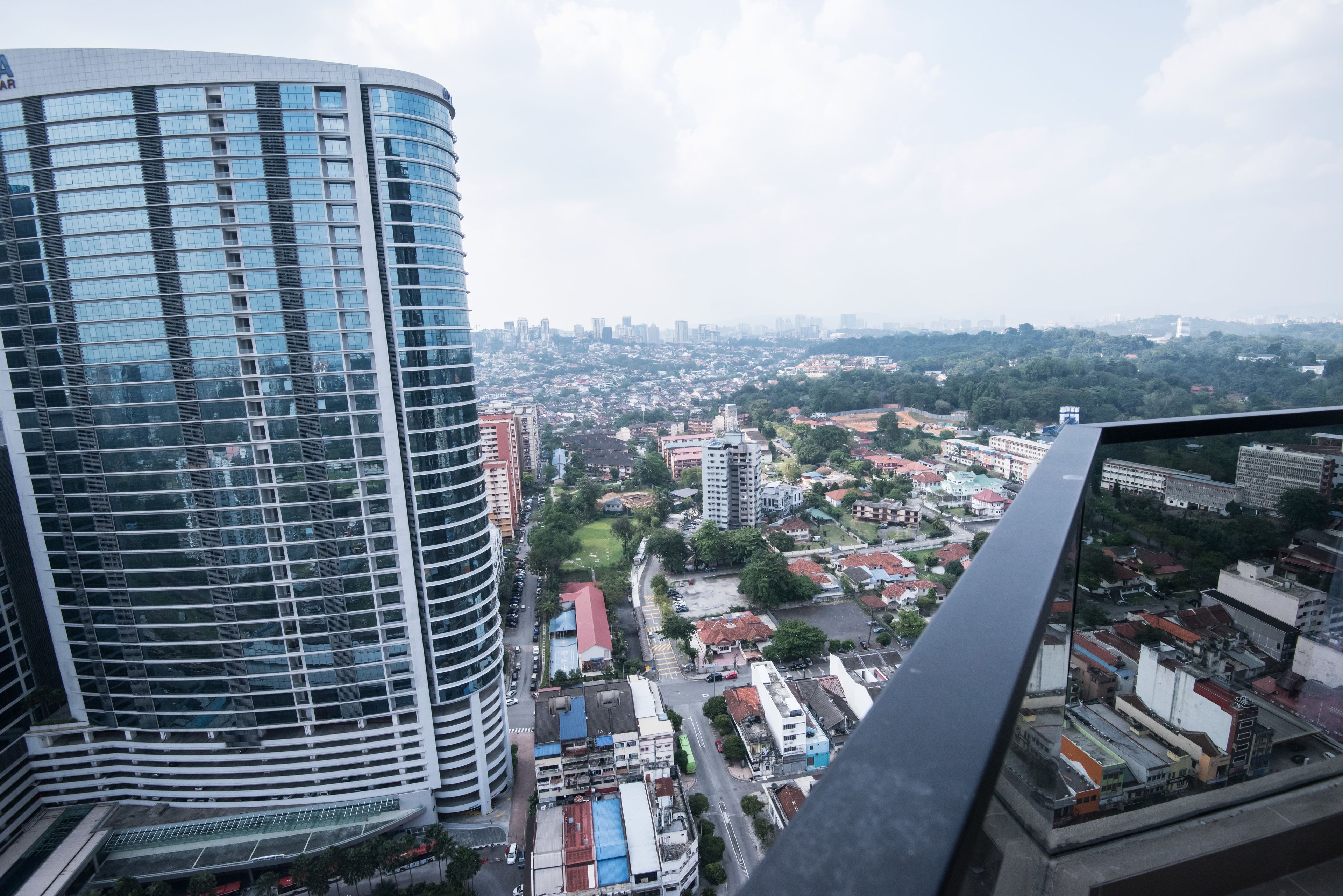 A high-rise building with a curved glass facade overlooking a cityscape with various buildings and greenery.