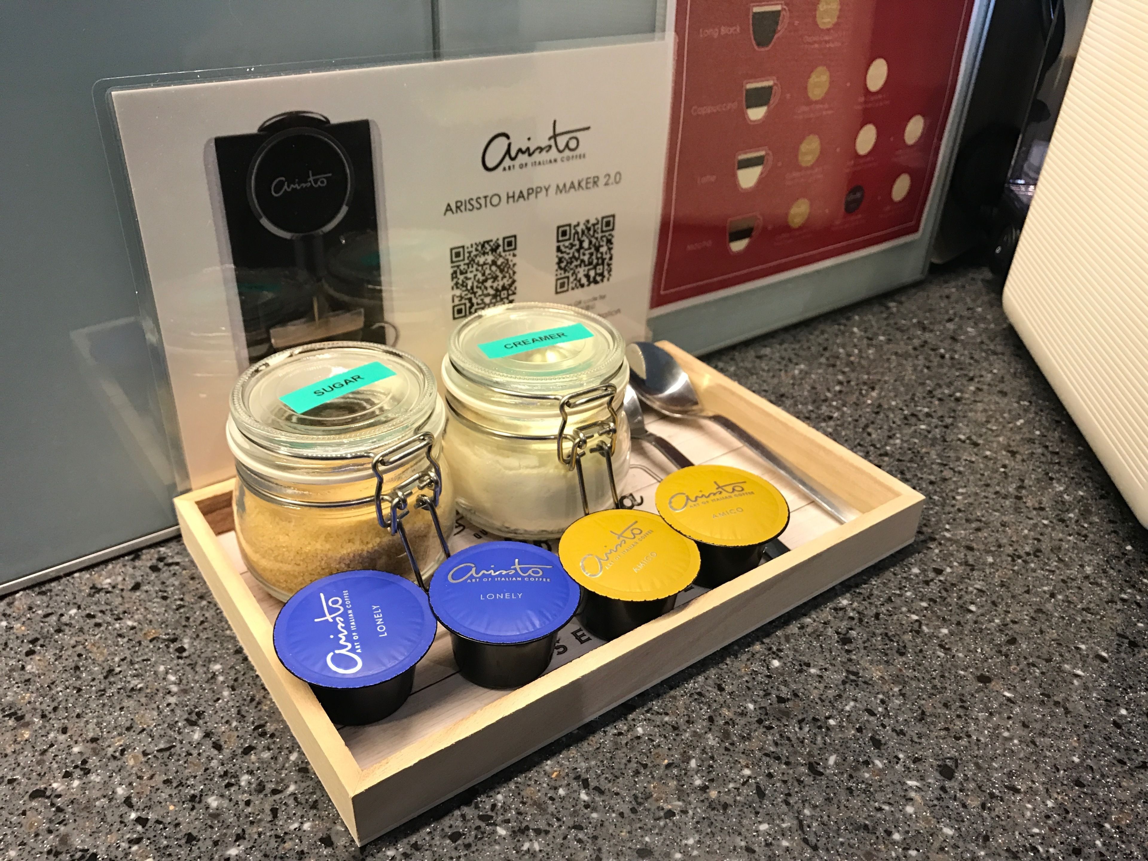 A tray with two jars labeled 'sugar' and 'cream', and two containers labeled 'Amico' with 'lonely' and 'art of italian coffee' on a countertop.