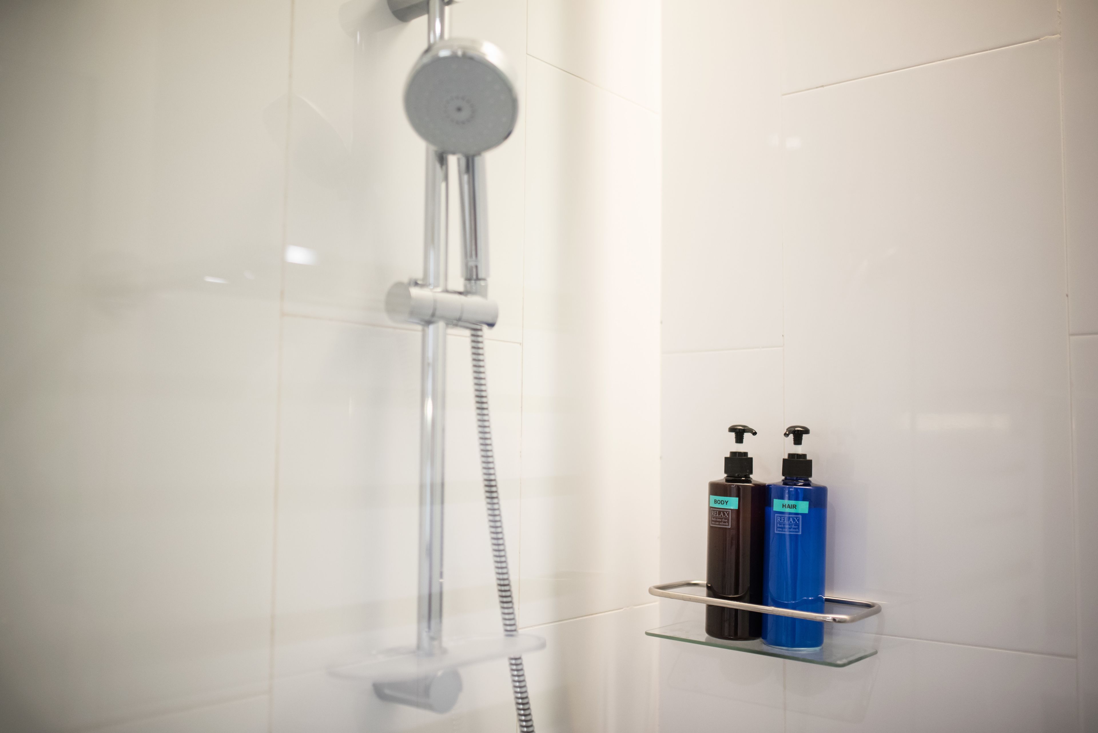 A modern bathroom with a glass shower enclosure, a chrome showerhead, and two bottles of shampoo and conditioner on a glass shelf.