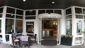 A reception area with a glass door, wicker furniture, and a brick floor. - Stadthotel Engel (Ettlingen)