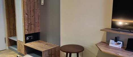 A hotel room with a bed, a wooden bench, a small table, a TV, and a wardrobe.