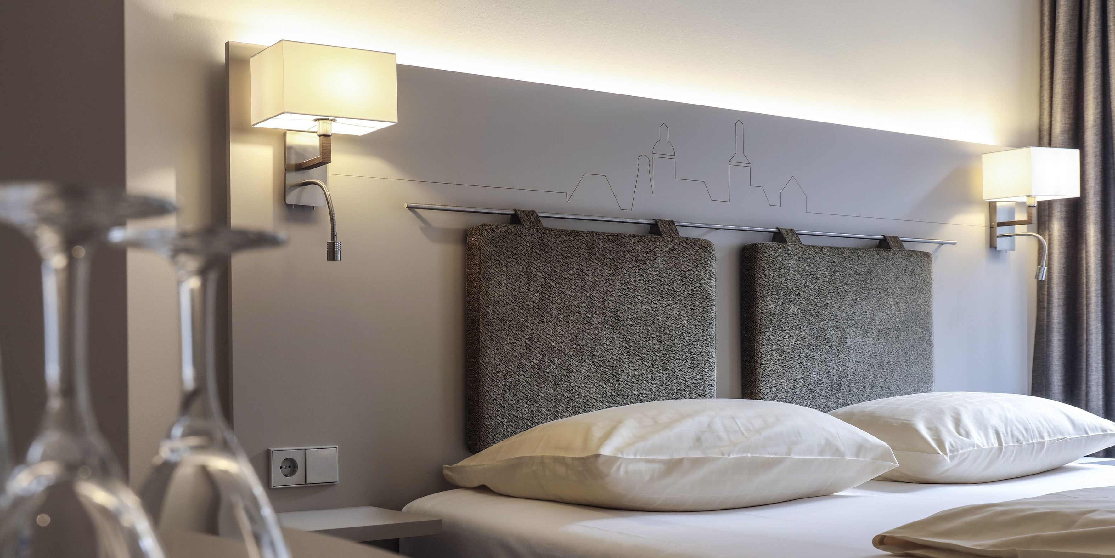 Hotelkamer met een bed, twee wandlampen, een stadsgezicht kunstwerk en een stopcontact.