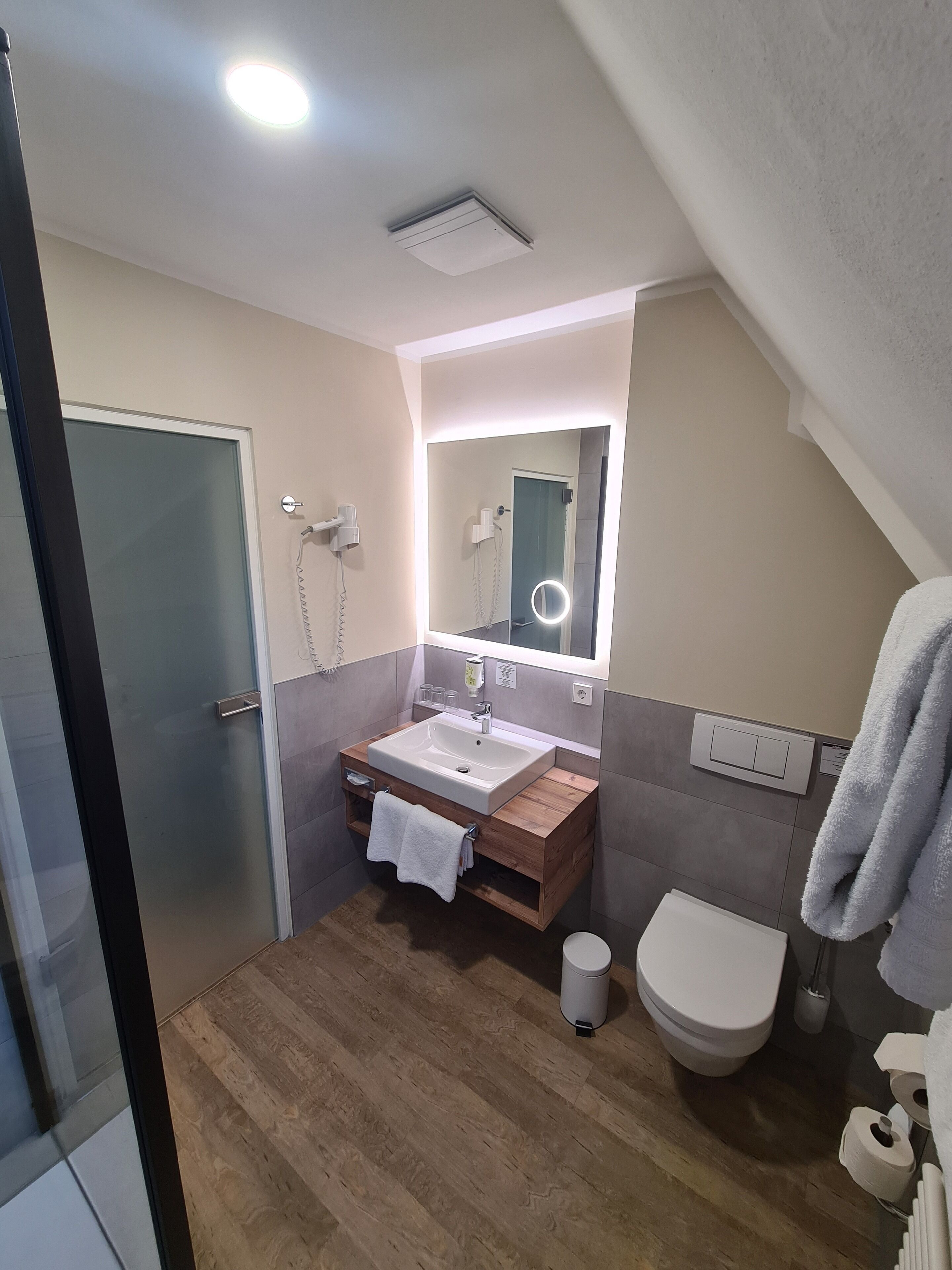 Un baño moderno con tocador de madera, un espejo grande, inodoro y zona de ducha.