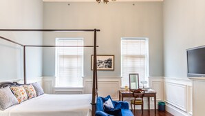 A bedroom with a four-poster bed, a desk with a chair, and a television on the wall. - Baan2459 Heritage House (Bangkok)