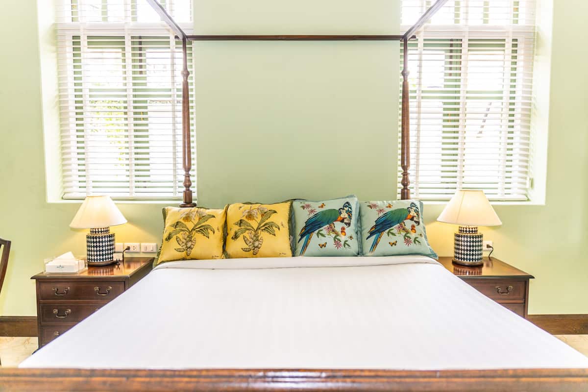 A neatly made bed with floral pillows, two bedside lamps, and a window with blinds.
