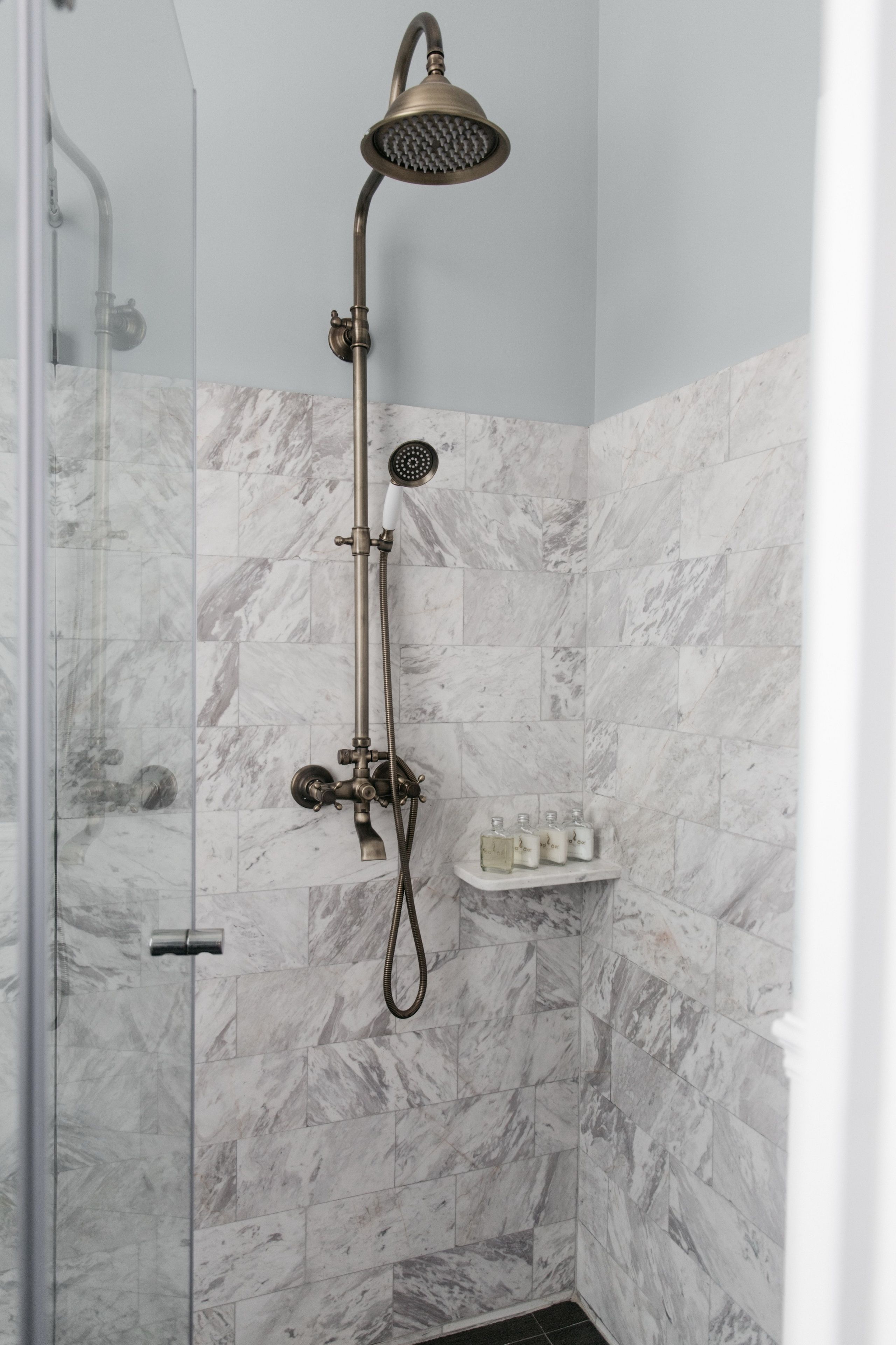 A shower with a handheld showerhead and a wall-mounted faucet, set against a marble wall.