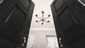 A view through open dark wooden doors towards a white ceiling with a chandelier. - Baan2459 Heritage House (Bangkok)