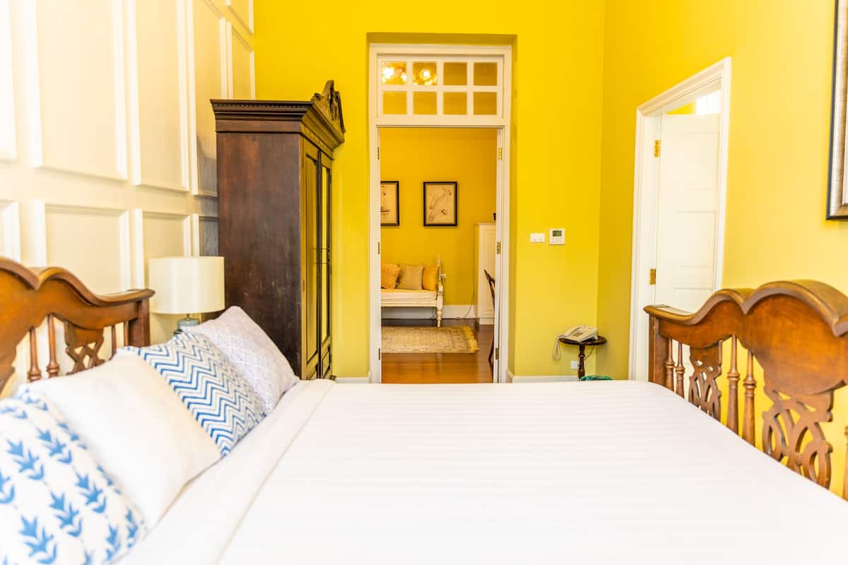 A bedroom with a large bed, wooden headboard, a nightstand, a lamp, and a door leading to another room.