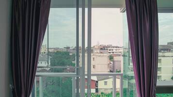 A room with a large window, curtains, and a view of buildings and greenery outside.