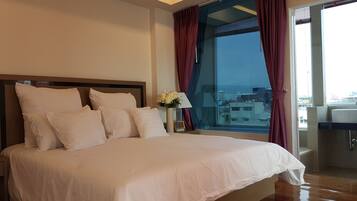 A bedroom with a large bed, a nightstand with a lamp, and a view of the city through a large window.