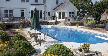A swimming pool with a deck, surrounded by potted plants and outdoor furniture.
