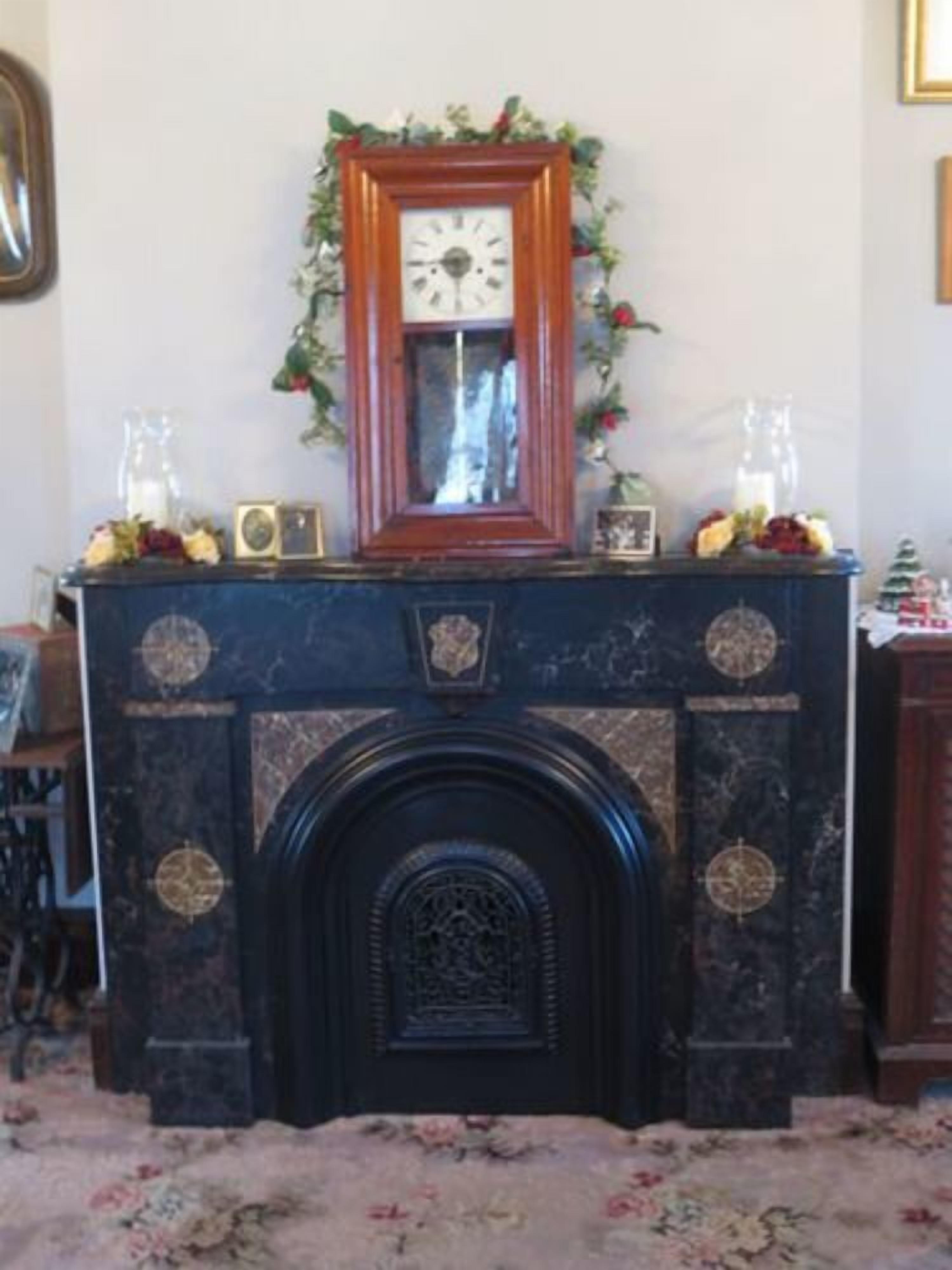 Una chimenea rodeada de objetos decorativos y un tapete floral, con un reloj encima.