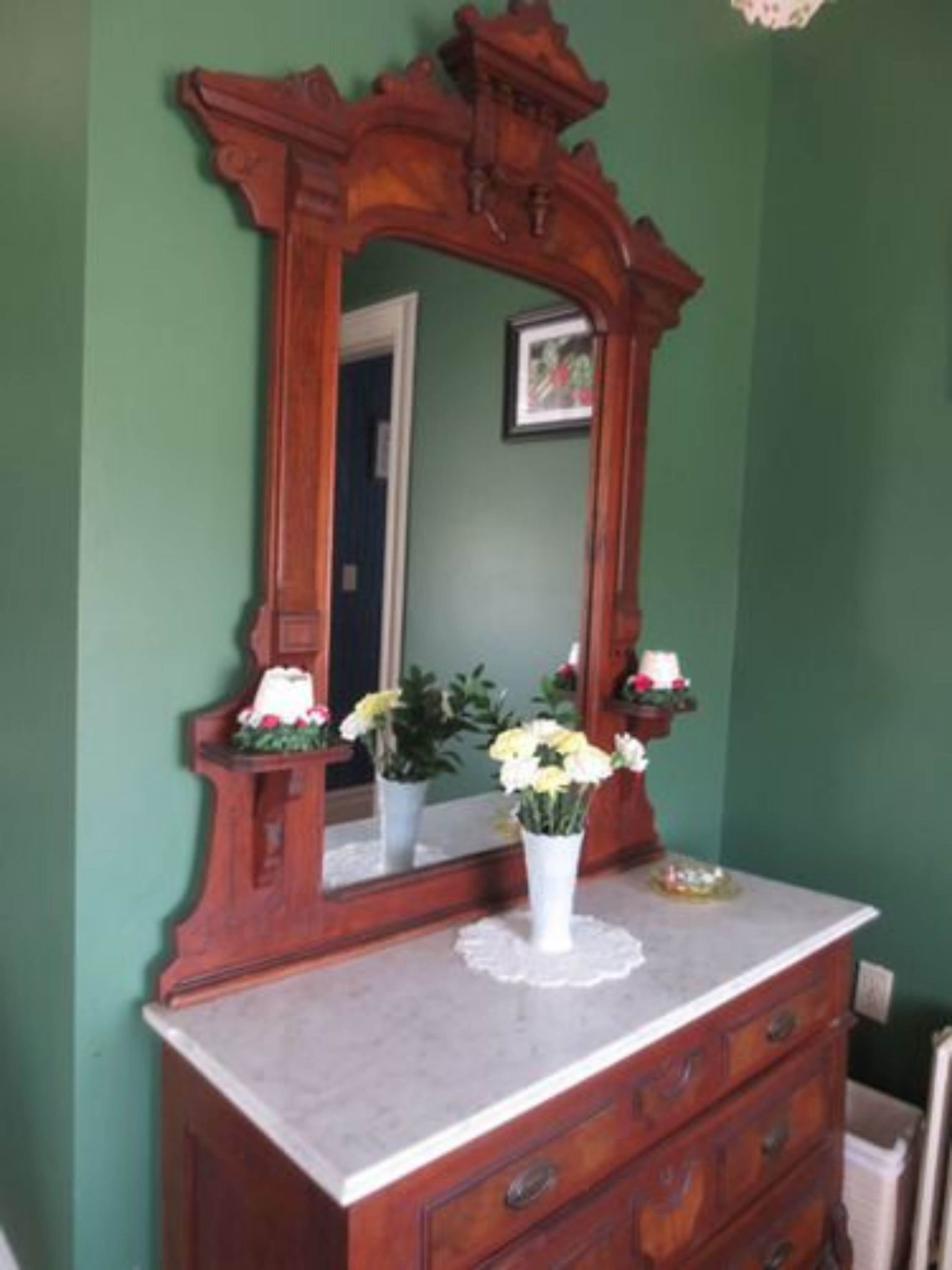 A wooden dresser with a marble countertop and a mirror above it. There are two potted plants on the countertop.