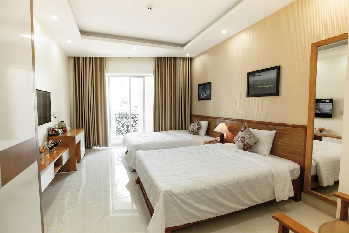 A hotel room with two beds, a TV, a desk, and a balcony.