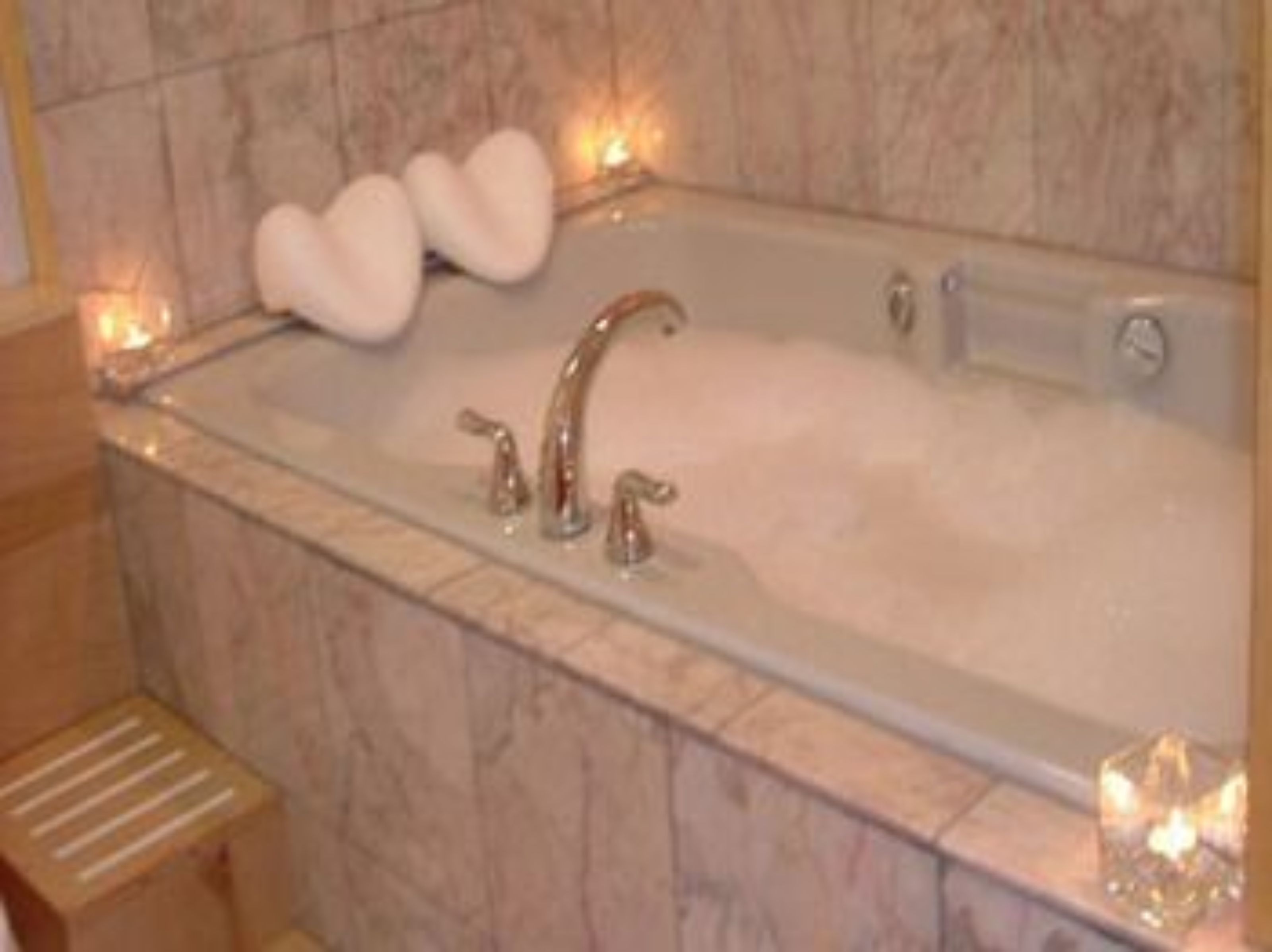 Une salle de bain en marbre avec une baignoire, deux robinets et des tapis de bain en forme de cœur.