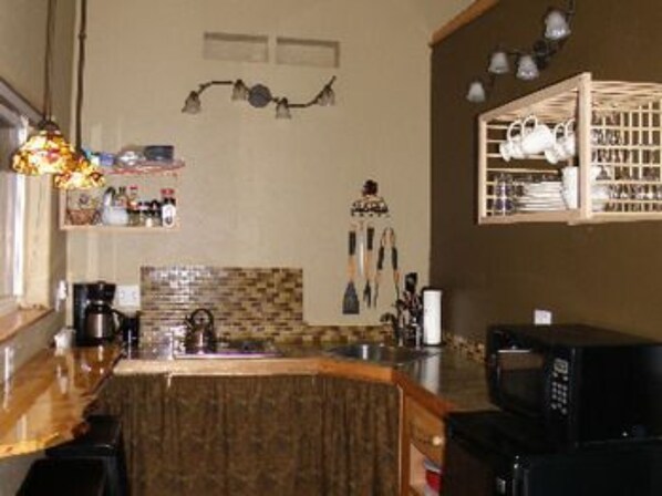 A kitchen with a wooden countertop, a coffee maker, a microwave, and a hanging light fixture. - Escape For Two B&B Guesthouse (Soldotna)